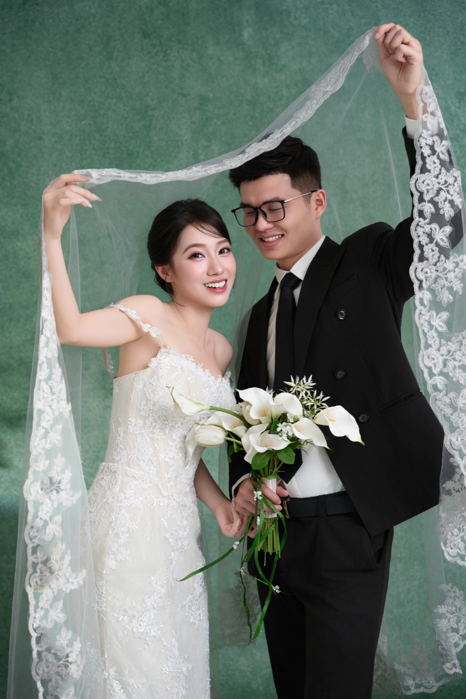 Đức Trịnh và Emi cùng nâng một tấm voan ren trên đầu, cười tươi